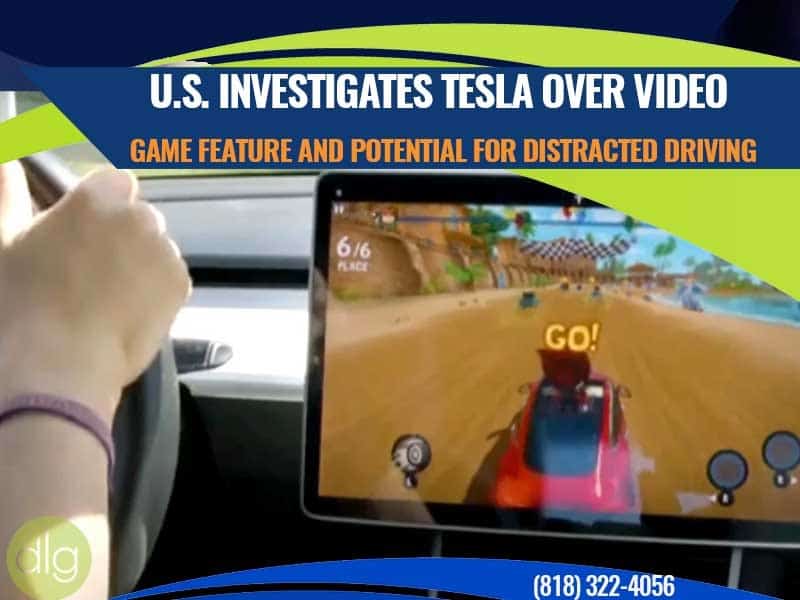 A person drives a Tesla while a video game is displayed on the car’s central touchscreen, with text about a U.S. investigation into potential distracted driving.
