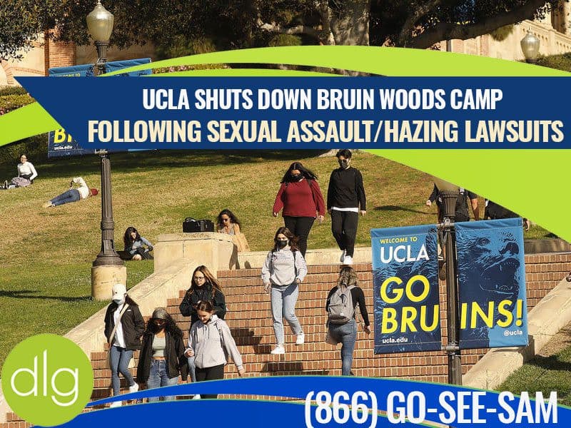 Several students walk on campus stairs at UCLA, with banners and a large headline announcing the shutdown of Bruin Woods Camp after sexual assault and hazing lawsuits.