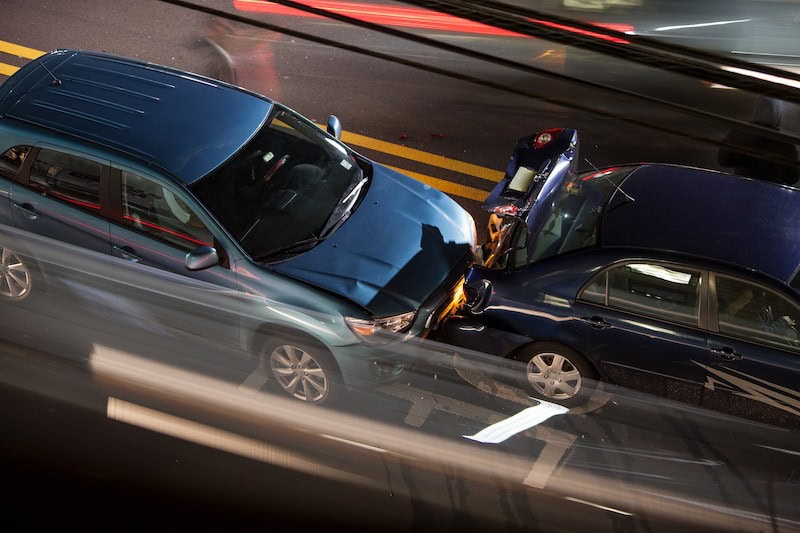 Two cars in a rear-end collision on a city street at night, with visible damage to the front of one car and the rear of the other.