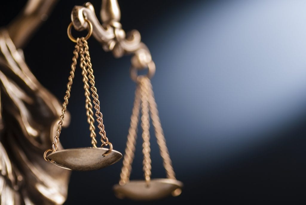 Close-up of a brass balance scale, symbolizing justice, set against a dark background with a beam of light illuminating part of the scene.